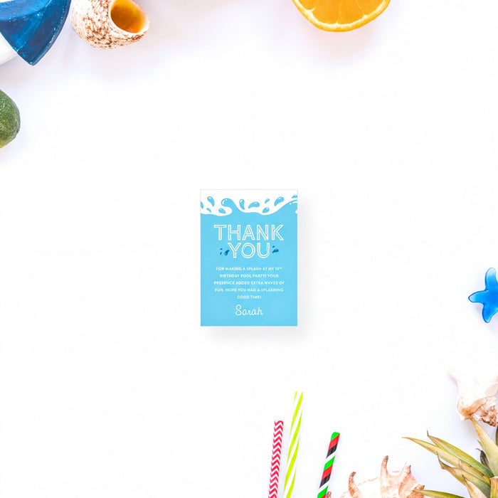 a blue "Thank You" card surrounded by various objects, including a blue seashell, an orange slice, and a straw wrapper.