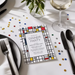 a colorful invitation card for a dinner party, with a table set with a wine glass, blackware, and confetti scattered around.