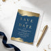 a blue and gold wedding invitation card with the text "Save the Date" and "Pacific Coast University Law School" printed on it, along with details about an upcoming event. The card is accompanied by a gold pen and scattered gold confetti on a white surface.