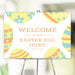 Colorful Easter Egg Hunt welcome sign with pastel yellow, blue, and orange Easter egg illustrations, displayed on an easel for a spring party or community event.