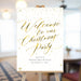 Christmas party welcome sign with gold script lettering on white background displayed on easel for holiday event entrance decor