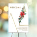 Elegant holiday welcome sign featuring poinsettia flowers, pinecones, berries, and a Christmas tree outline, ideal for seasonal party decor.