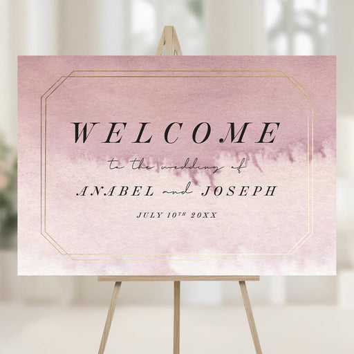 Romantic wedding welcome sign with mauve watercolor background, faux gold border, and personalized with names and wedding date on easel.