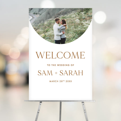 Minimalist wedding welcome sign featuring couple's photo, personalized names, and wedding date, displayed on an easel.