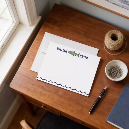 a wooden desk with a white card, a pen, a bowl of clips, and a window.