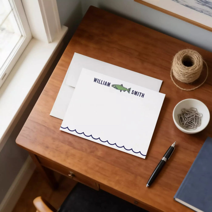 a wooden desk with a white card, a pen, a bowl of clips, and a window.