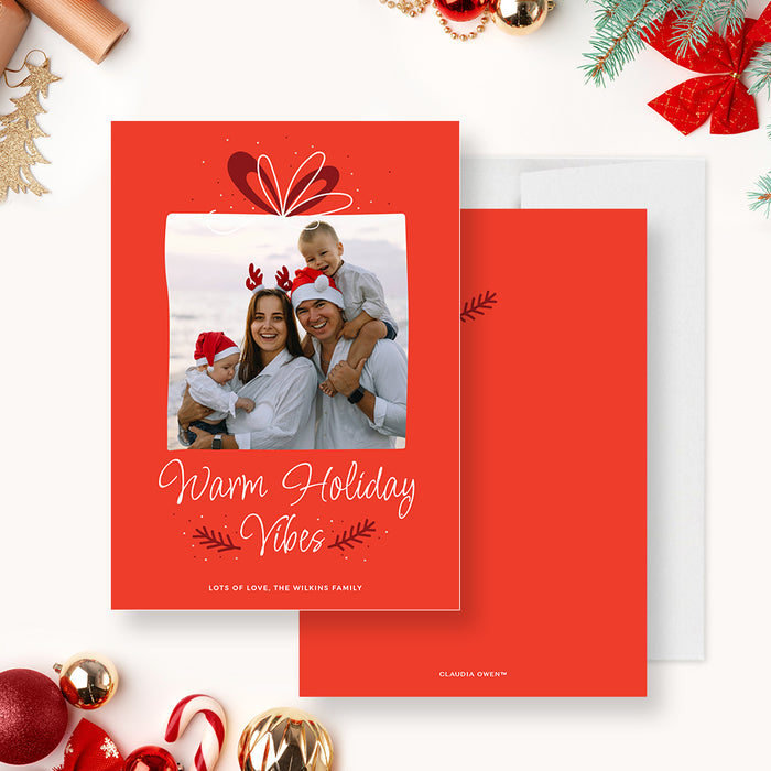 Family holiday photo card template featuring a red background, gift bow illustration, framed family photo and Warm Holiday Vibes greeting in a festive Christmas design