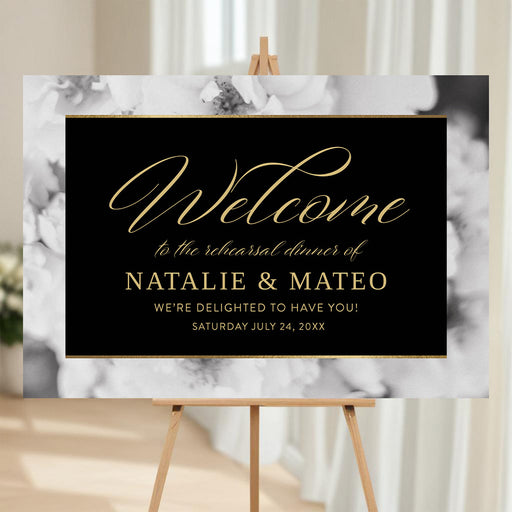 rehearsal dinner welcome sign on an easel, featuring gold script on a black background with a black and white floral border
