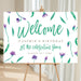 Floral birthday welcome sign with purple flowers, green leaves, and personalized garden party celebration text.