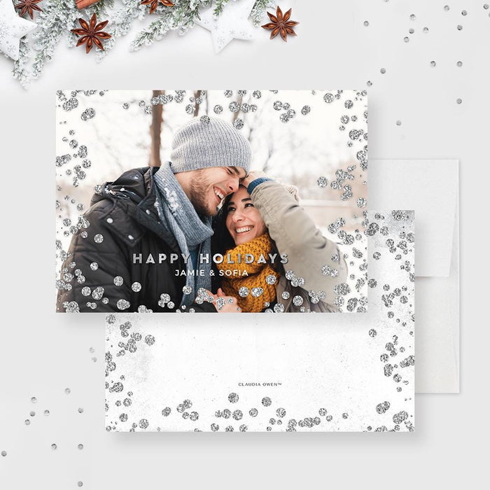 Modern holiday photo card featuring a smiling couple in winter attire surrounded by silver glitter accents and “Happy Holidays” text.