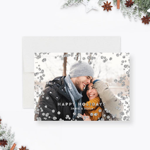 Modern holiday photo card featuring a smiling couple in winter attire surrounded by silver glitter accents and “Happy Holidays” text.