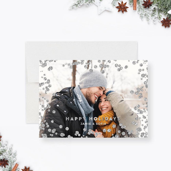 Modern holiday photo card featuring a smiling couple in winter attire surrounded by silver glitter accents and “Happy Holidays” text.