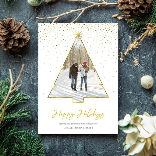 Elegant holiday photo card featuring a gold-outlined Christmas tree photo frame, gold confetti accents and modern script Happy Holidays typography on a white background.