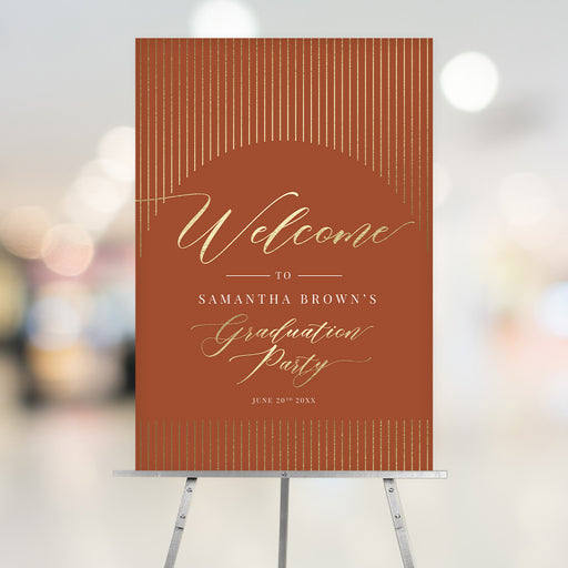 Terracotta and gold graduation party welcome sign personalized with the graduate’s name and date, displayed on an easel for an elegant event entrance.