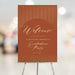 Terracotta and gold graduation party welcome sign personalized with the graduate’s name and date, displayed on an easel for an elegant event entrance.
