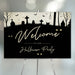 Halloween party welcome sign with a spooky graveyard silhouette, bats, glowing eyes, and elegant script text on a black background