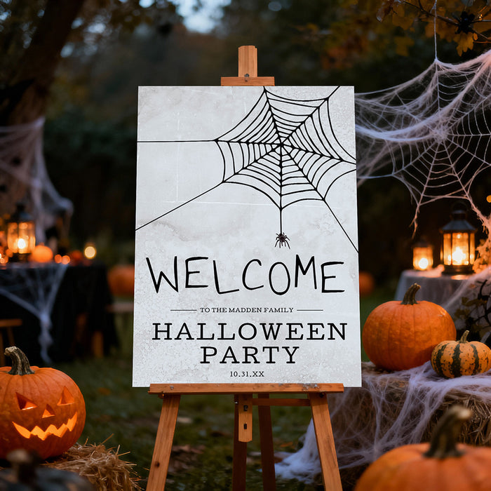 Halloween welcome sign with a spooky spider web design, hanging spider, and party wording displayed on an easel