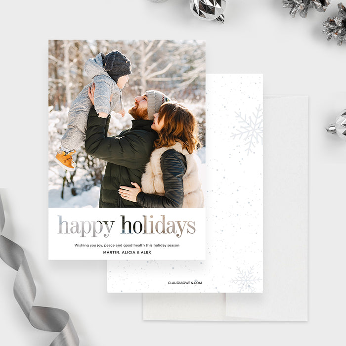 Digital holiday greeting card featuring a modern minimalist layout with a large family winter photo on top, elegant serif Happy Holidays text at the bottom, and a clean white background surrounded by festive silver ornaments.