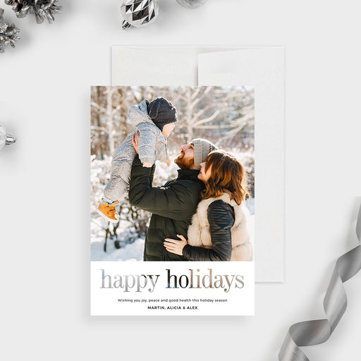 Digital holiday greeting card featuring a modern minimalist layout with a large family winter photo on top, elegant serif Happy Holidays text at the bottom, and a clean white background surrounded by festive silver ornaments.