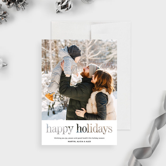 Digital holiday greeting card featuring a modern minimalist layout with a large family winter photo on top, elegant serif Happy Holidays text at the bottom, and a clean white background surrounded by festive silver ornaments.
