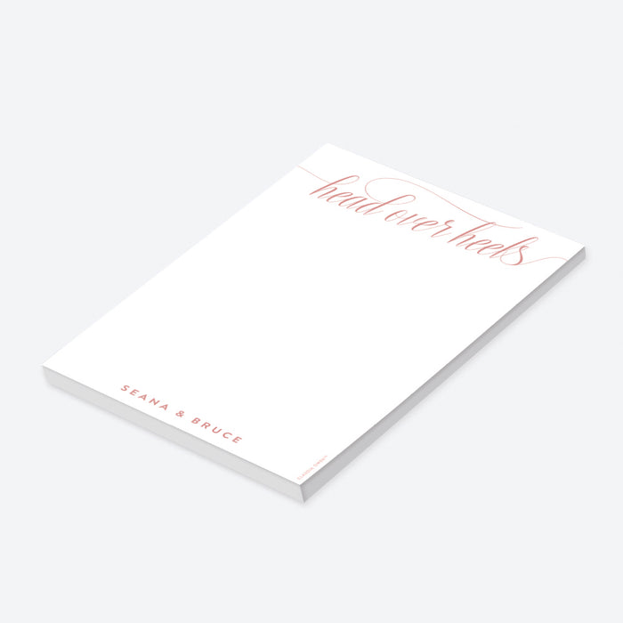 Personalized blush notepad featuring “head over heels” script with couple’s name at the bottom in elegant lettering-side