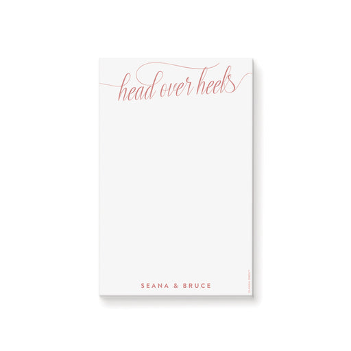 Personalized blush notepad featuring “head over heels” script with couple’s name at the bottom in elegant lettering