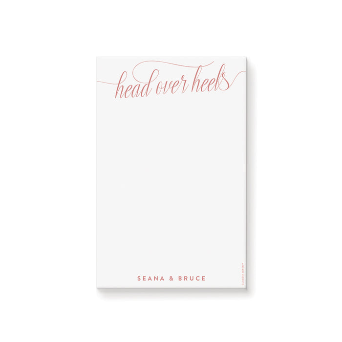 Personalized blush notepad featuring “head over heels” script with couple’s name at the bottom in elegant lettering
