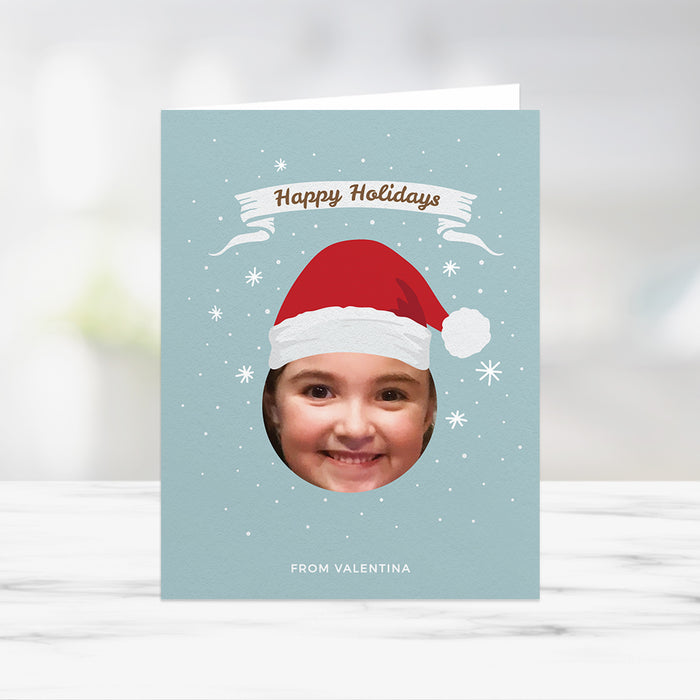 Kids holiday photo card template featuring child photo cutout, Santa hat illustration, snowflake background and Happy Holidays text in a festive digital Christmas design