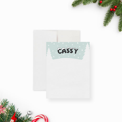 Personalized kids note card with snowy winter scene, snowflakes, pine trees, and custom name in snow lettering-front