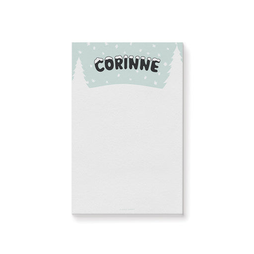 Personalized kids notepad with snowy winter scene, pine trees, snowflakes, and custom name in playful snow-topped lettering.