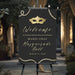 Personalized masquerade welcome sign featuring a gold mask, a black background, elegant lettering, and bead accents, displayed on an easel for a Mardi Gras ball.