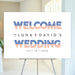 Modern wedding welcome sign with orange and blue striped accents and minimalist typography displayed on an easel.