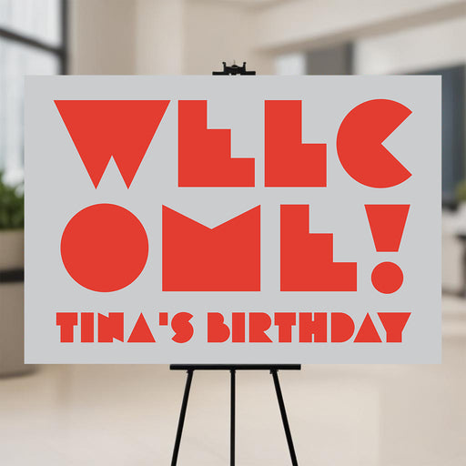 modern birthday party welcome sign with bold red lettering, gray background, and personalized birthday party wording displayed on an easel