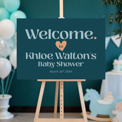 Personalized baby shower welcome sign with dark teal background, pale blue lettering, peach heart, honoree’s name and event date