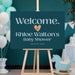 Personalized baby shower welcome sign with dark teal background, pale blue lettering, peach heart, honoree’s name and event date
