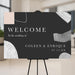 Modern abstract wedding welcome sign with black background and minimalist shapes displayed on easel.