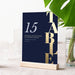 Navy blue table number 15 card with vertical gold Table lettering in a wooden holder.