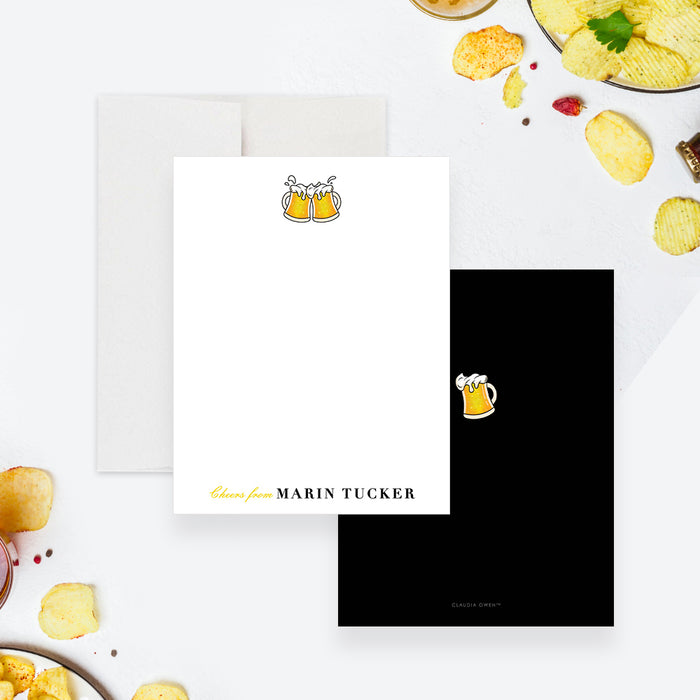White personalized note card with clinking yellow beer mugs, beside a black back with a small beer mug illustration.