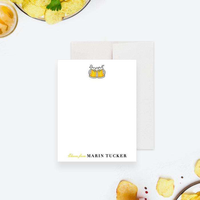 White personalized note card with clinking yellow beer mugs, beside a black back with a small beer mug illustration.
