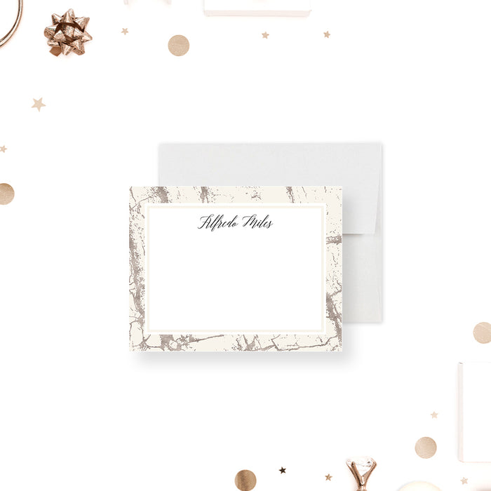 Personalized note card with a white writing area with a beige and printed silver marble border and a name in script. Shown with a white envelope.