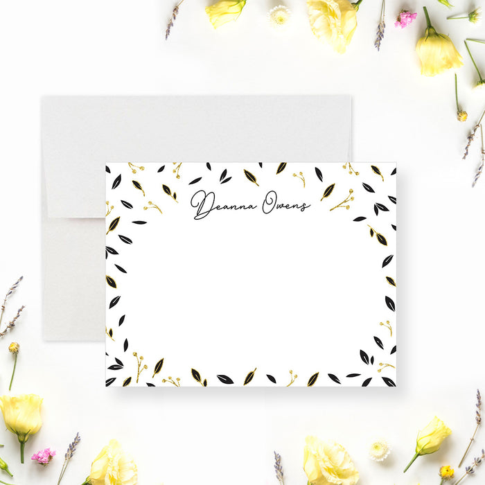 Personalized note card with a white front framed by scattered black and printed gold leaves with a personalized name. Shown with a white envelope.