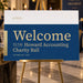 Blue and gold charity ball welcome sign on an easel with a logo area and personalized event details