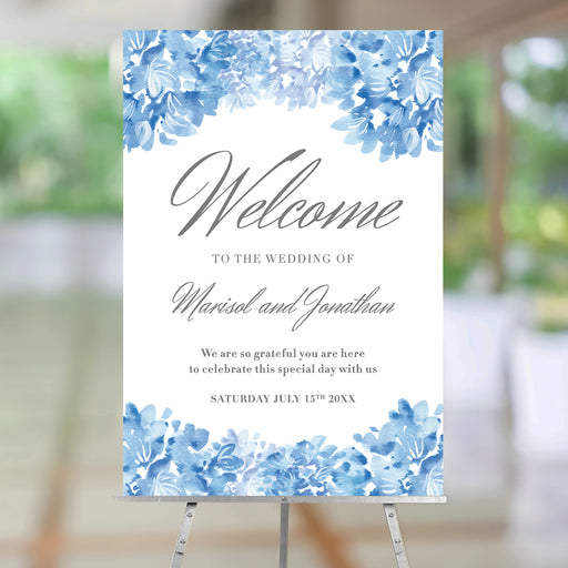 Personalized blue watercolor hydrangea wedding welcome sign with gray script lettering, couple’s names, wedding date, and floral borders displayed on an easel