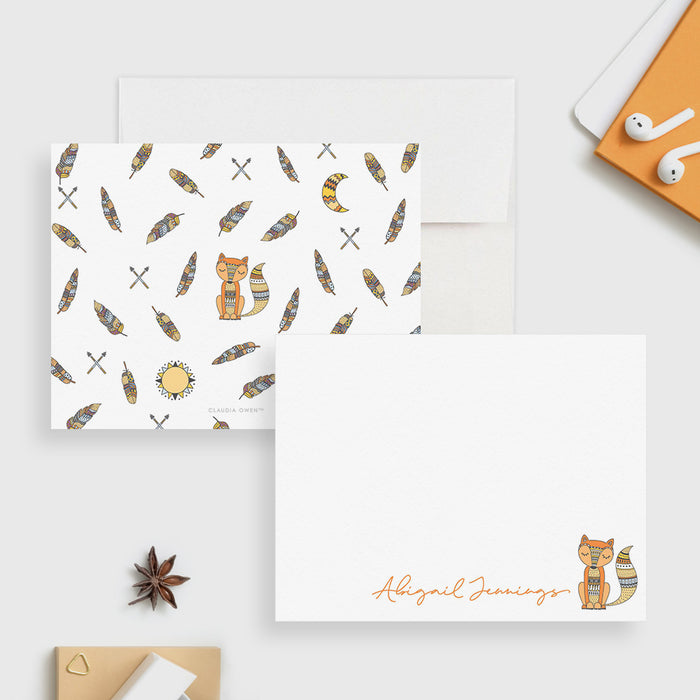 White personalized note card with a fox illustration, beside a back patterned with feathers, arrows and sun and moon motifs.