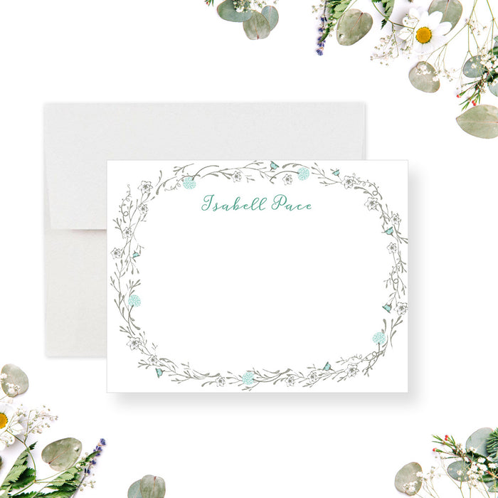 Personalized note card with a white front with a delicate botanical border and a personalized name in pale blue-green script. Shown with a white envelope.