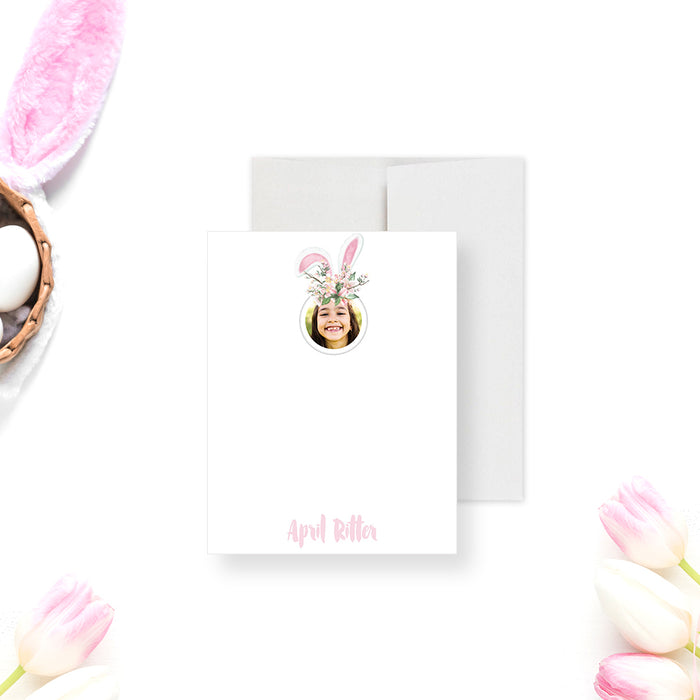 Personalized note card with a white front with a round photo, floral bunny ears, and a name in pink script. Shown with a white envelope.