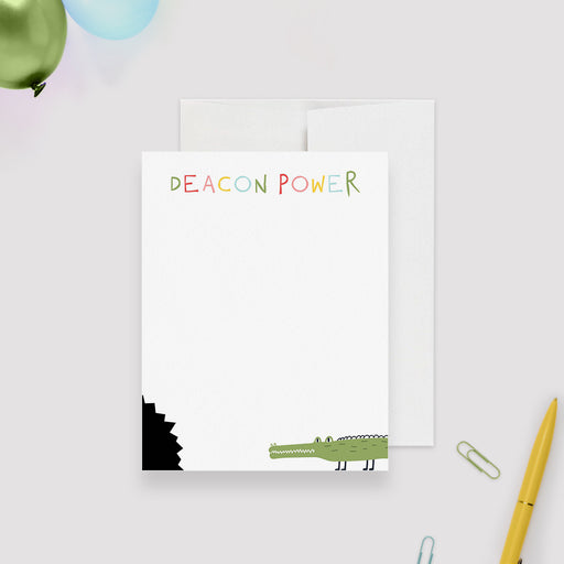 Personalized white note card with a green crocodile carrying blue and yellow balloons and a black printed bite-mark corner.