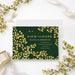 Personalized emerald green wedding save the date card with gold-colored leaf vines, couple’s monogram, names, wedding date and location-front