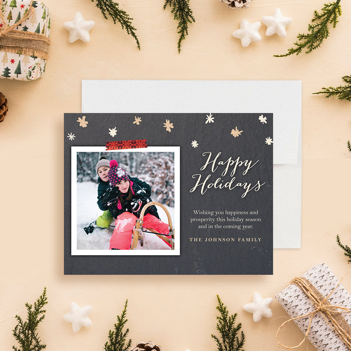 Personalized family photo holiday card with a winter sledding photo, cream snowflakes and Happy Holidays greeting on a charcoal background-front