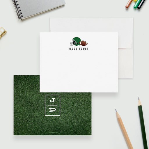 Personalized football note cards with a helmet and ball on the white front and a white monogram on the green grass patterned reverse.